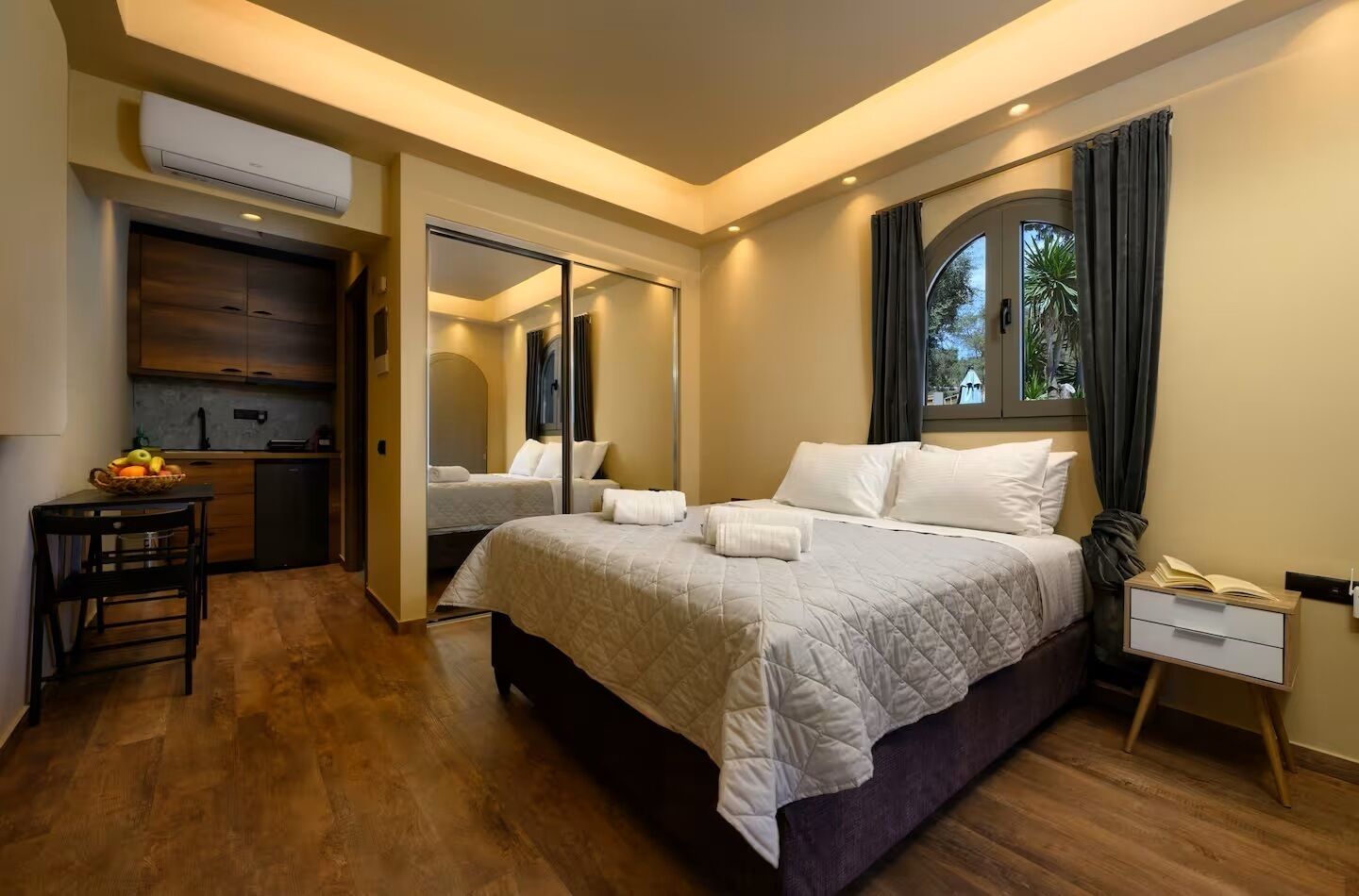 A modern hotel room with a large bed, a desk, and a small kitchenette.