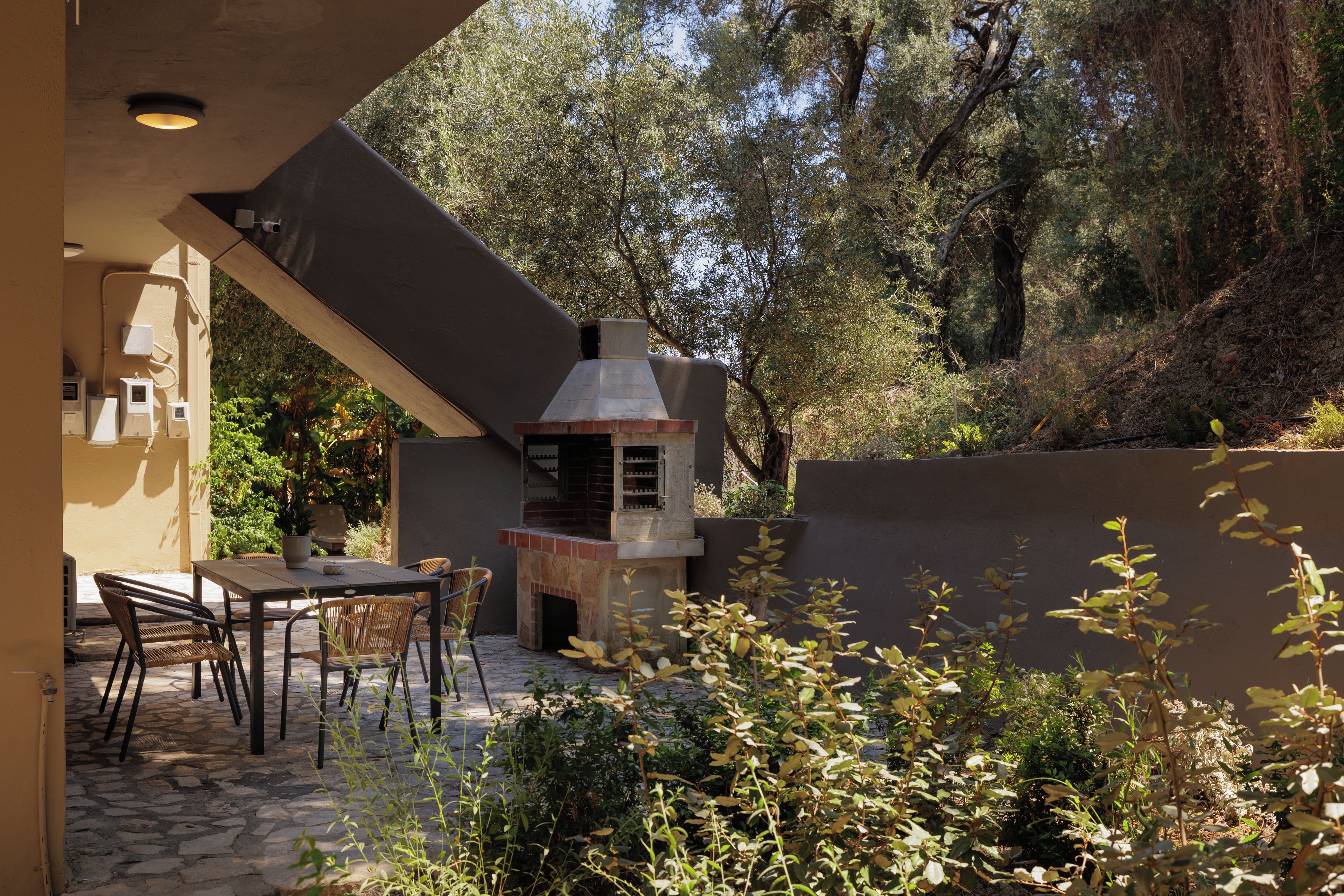 An outdoor patio with a stone table and chairs, a barbecue grill, and a view of a wooded hillside.