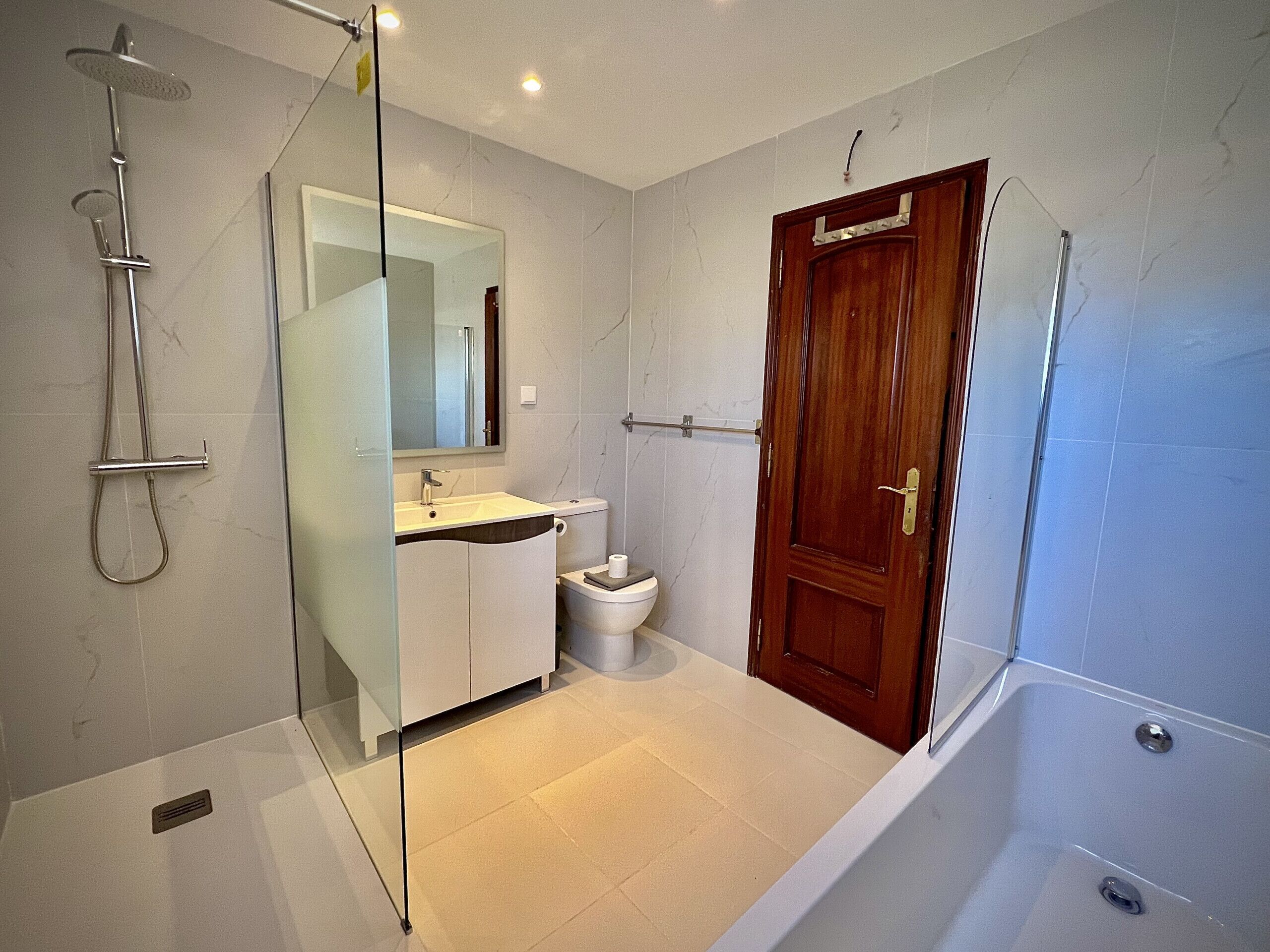 Ein modernes Badezimmer mit einer gläsernen Dusche, einem weißen Waschbecken und einer Holztür.