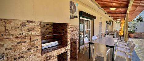 An outdoor patio with a brick fireplace, a dining table, and chairs.