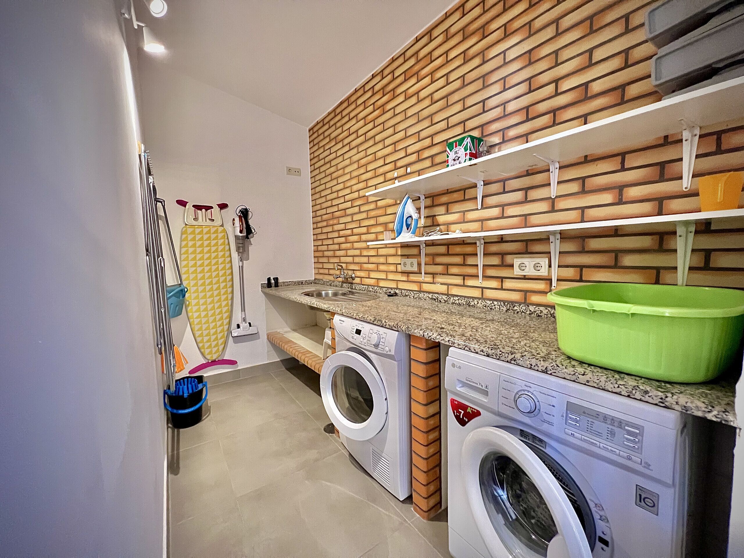 A laundry area with two washing machines, a sink, and a brick-patterned wall.