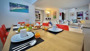 Uma área de refeições com uma mesa de madeira posta para o café da manhã, incluindo pratos, talheres e um jarro de suco de laranja.