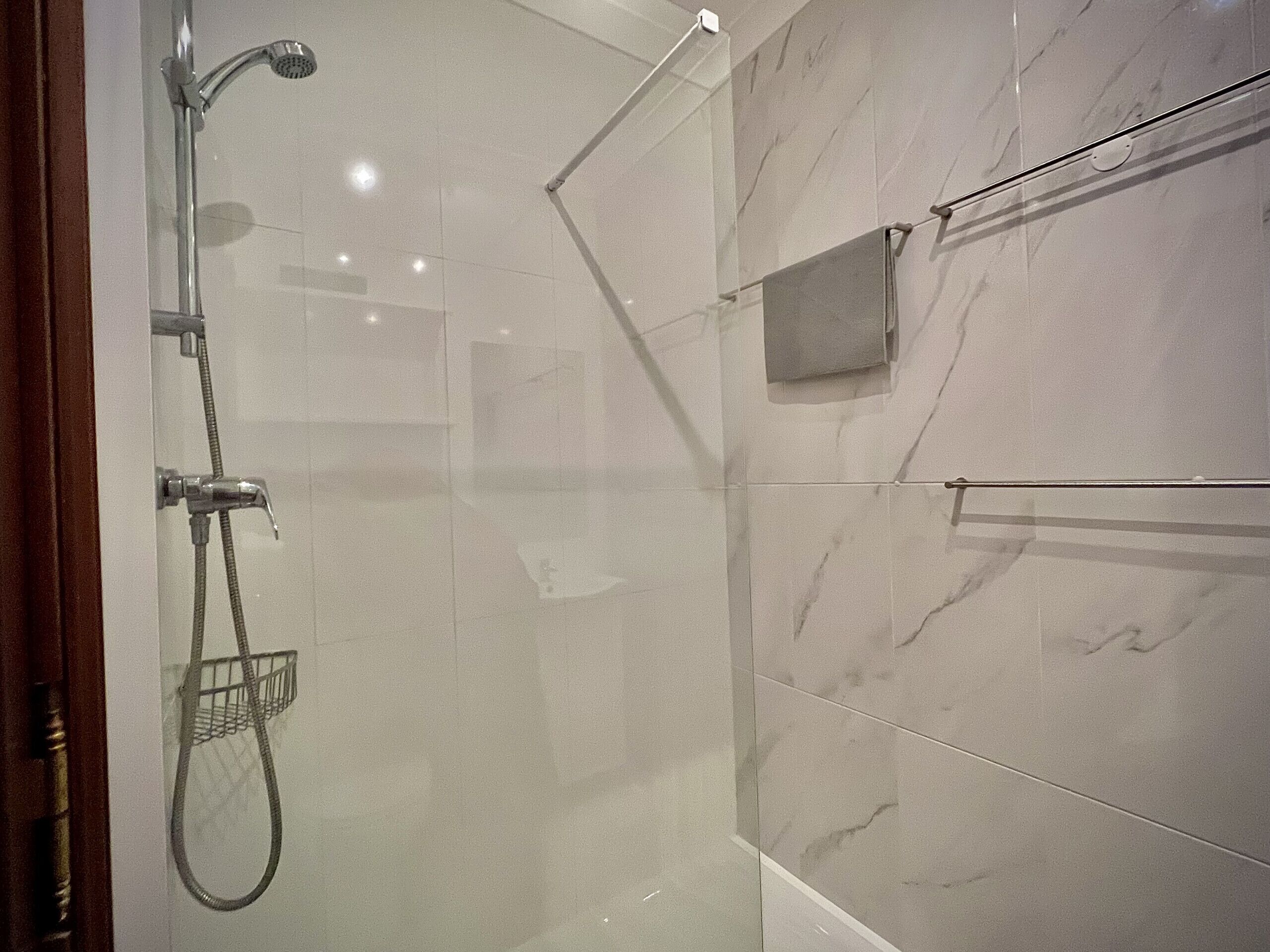 Ein modernes Duschbad mit Glastür, Handbrause, einem Haken zur Handtuchaufhängung und einem kleinen Spender für Handtücher.