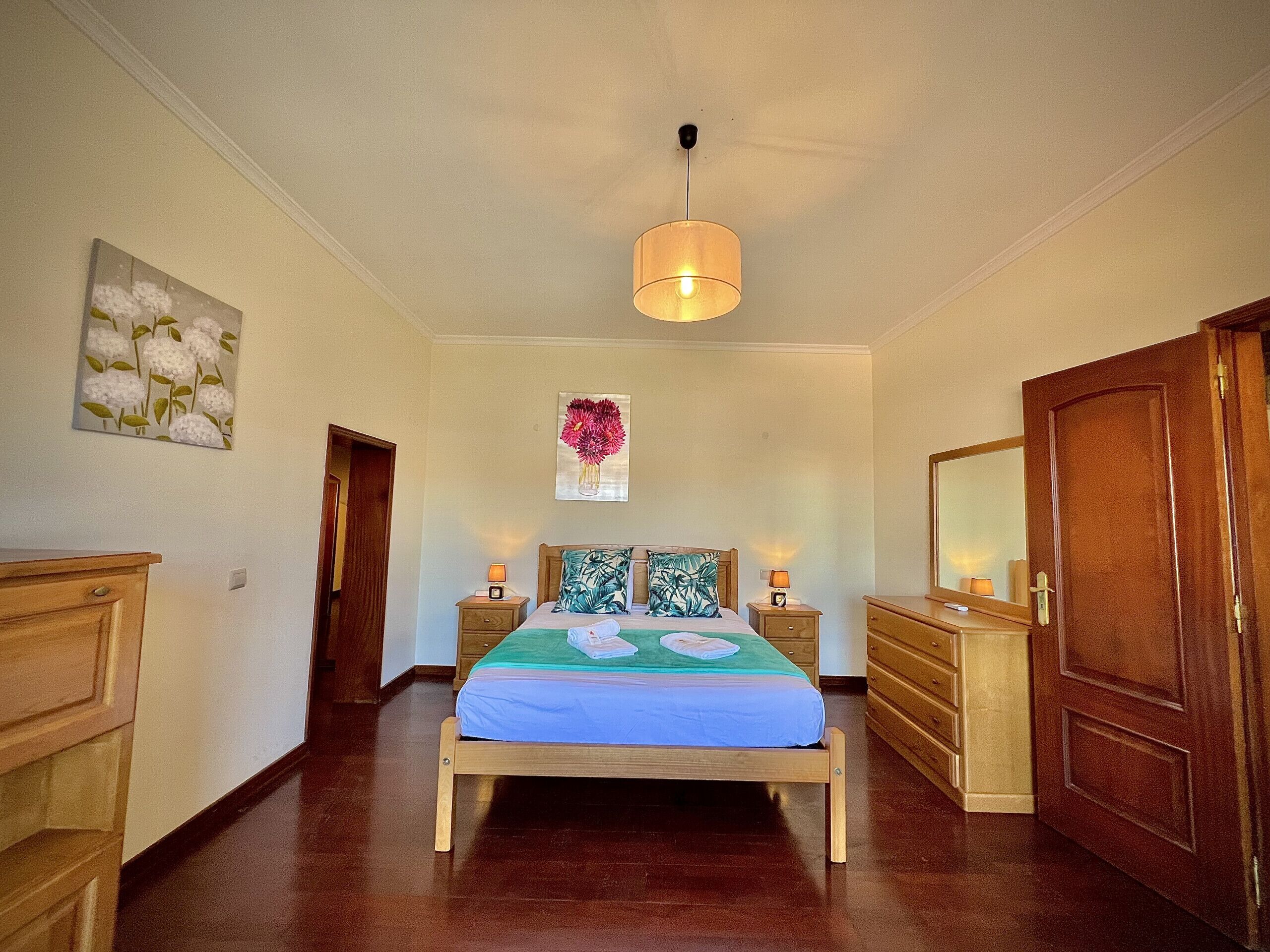Une chambre à coucher avec un lit en bois, des tables de chevet, une lampe suspendue et des œuvres d’art accrochées aux murs.