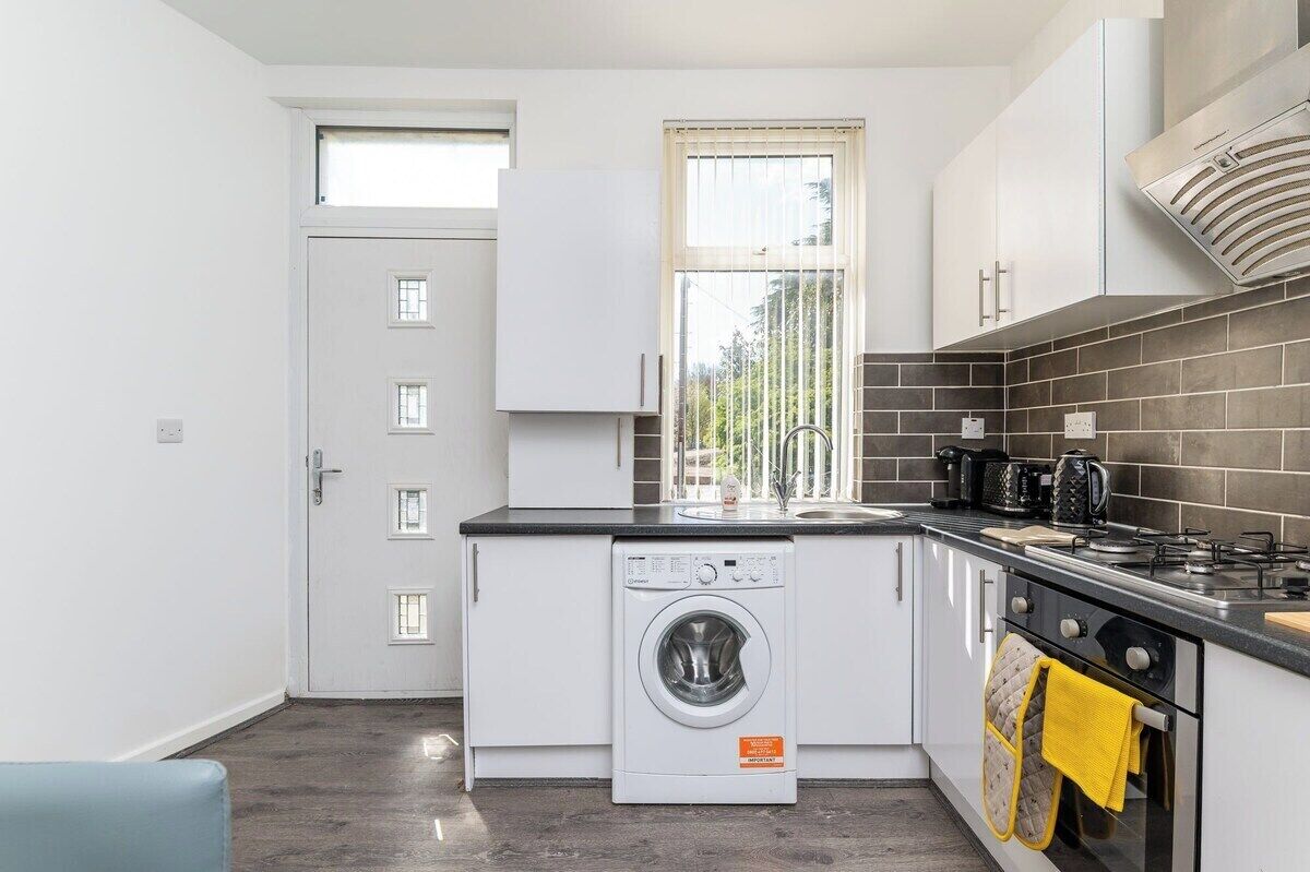 Una cocina compacta con lavadora integrada, una ventana con persianas, estufa y fregadero.