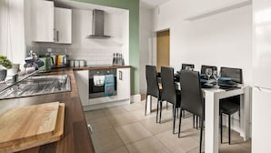 A modern kitchen with white cabinets, a built-in oven, and a dining area with black chairs and a white table.