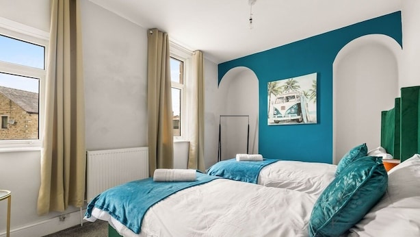 A bedroom with two beds, a window, a radiator, and a painting on the wall.
