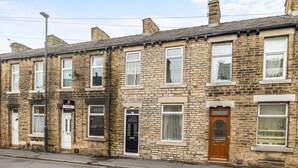 A row of terraced houses with stone facades, white-framed windows, and a 'For Sale' sign.