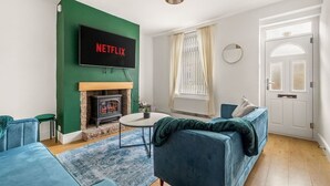 A living room with a fireplace, a blue sofa, a TV mounted on a green wall, and a door with a frosted glass panel.
