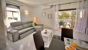 Ein modernes Wohnzimmer mit einem grauen Ecksofa, einem Couchtisch und einem Essbereich mit gedecktem Frühstückstisch.
