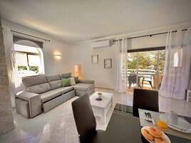 Uma sala de estar moderna com um sofá modular cinza, uma mesa de centro e uma área de jantar com mesa posta para o café da manhã.