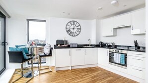 A modern kitchen with white cabinets, a black countertop, a stainless steel oven, and a large wall clock. - Yorksha Luxury Apartments | Leeds City | Balcony (West Yorkshire)