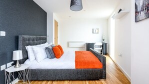 A modern bedroom with a large bed, a desk, and a chair. - Yorksha Luxury Apartments | Leeds City | Balcony (West Yorkshire)