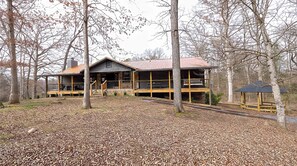 Eine Holzhütte mit Veranda, überdachter Terrasse und kleinem Pavillon in bewaldeter Landschaft.