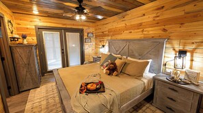 Ein Schlafzimmer in einer Holzhütte mit einem Bett, Nachttischen, einer Kommode und einem Deckenventilator.