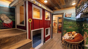 Quarto estilo cabana com piso de madeira, cama com cabeceira vermelha, uma pequena janela e parede com mural.