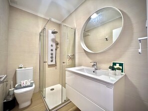 A modern bathroom with a glass-enclosed shower, a white sink with a mirror above, and a toilet with toilet paper and a hand dryer. - Vilamoura Eden Villa With Pool by Homing (Loulé)