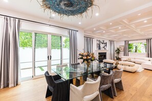 Un salon spacieux avec une table à manger en verre, des canapés gris et blancs et une cheminée.