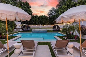 Un espace piscine agrémenté de chaises longues et de parasols, entouré de verdure et illuminé de guirlandes lumineuses.