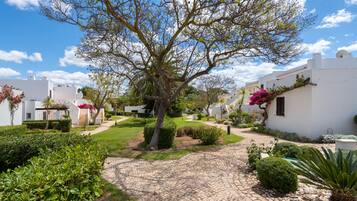 Un patio con sendero adoquinado, rodeado de edificios blancos con balcones y macetas con plantas.