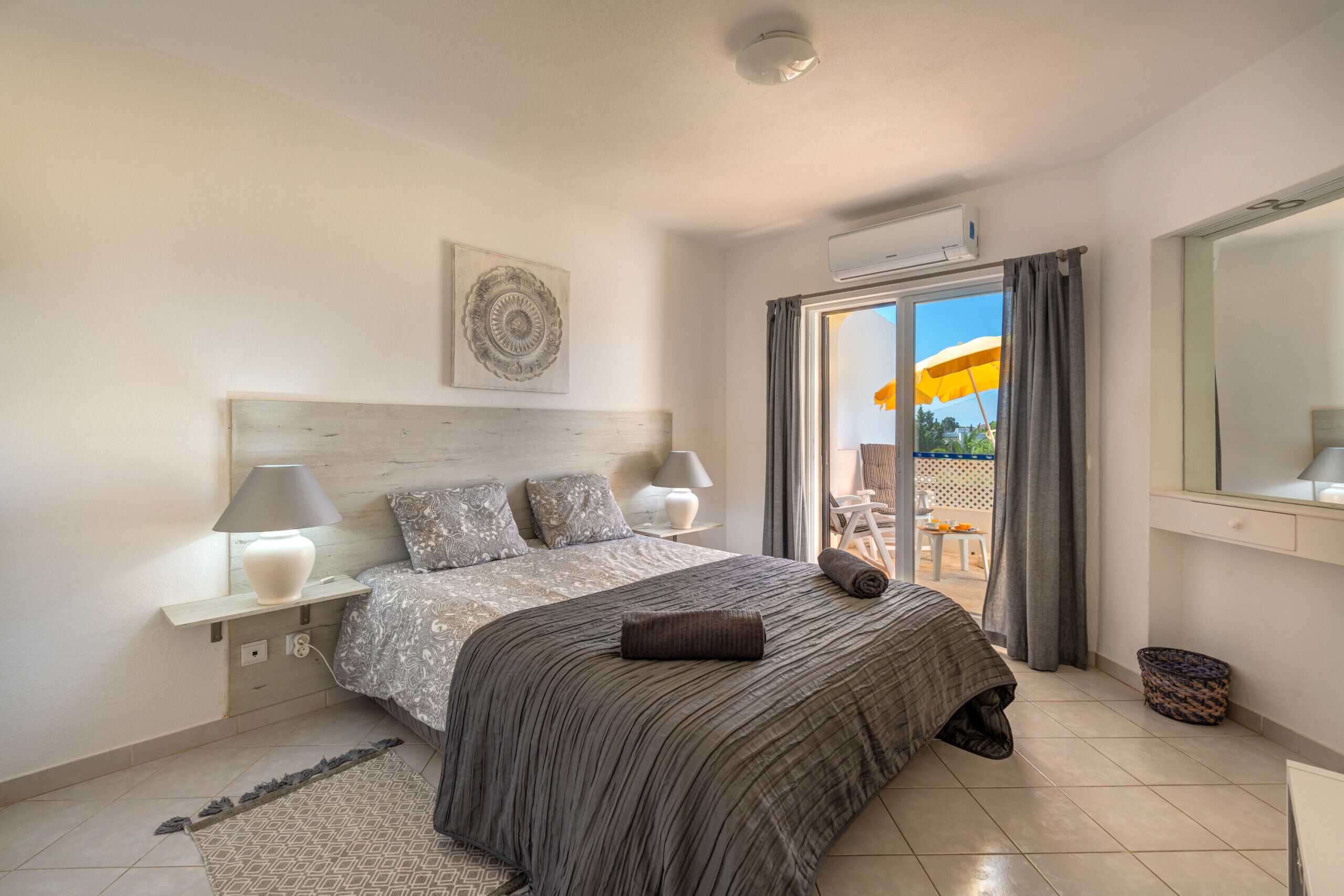 Un dormitorio con cama, lámparas de noche, cabecero, ventana con cortinas y vistas al exterior.