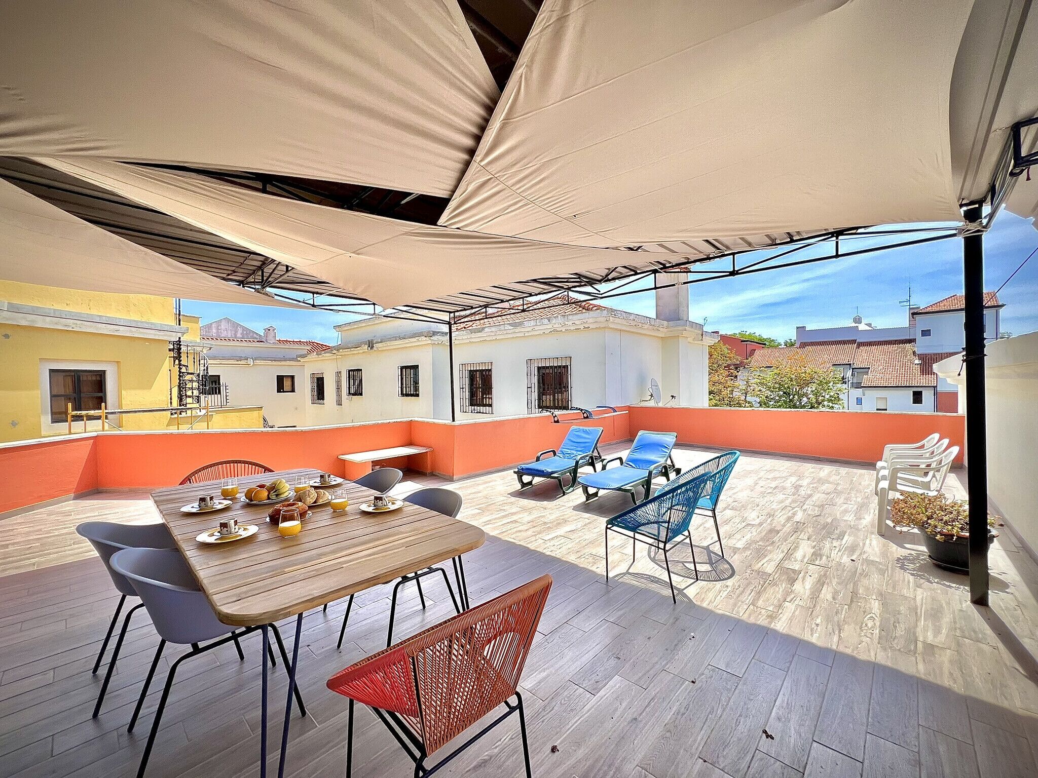 A rooftop patio with a table set for dining, lounge chairs, and a large umbrella providing shade.