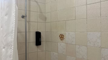 Una dutxa amb cortina, un vàter de mà i un dosificador de sabó fixat a la paret.
