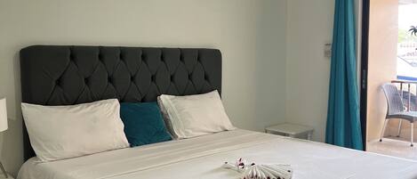 A neatly made bed with a tufted headboard, white bedding, and a towel with rose petals.