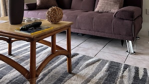 Een woonkamer met een paarse bank, een houten salontafel en een vaas met gedroogde bloemen.
