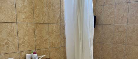 Ein Badezimmer mit Toilette, Duschvorhang, Korb mit Toilettenartikeln und Mülleimer.