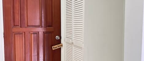 A wooden door with a 'Please Service' sign, a white closet with louvered doors, and a tiled floor.