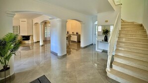 Un hall d’entrée spacieux avec un sol en marbre, des colonnes blanches et un escalier.