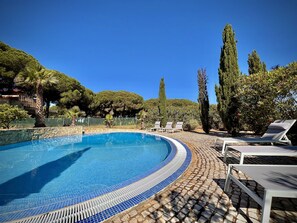 A curved swimming pool with tiled edges, surrounded by lounge chairs and tall trees. - Quarteira Premium Villa by Homing (Loulé)