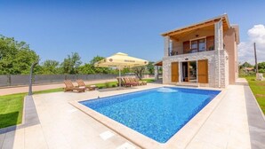 A modern house with a swimming pool, a covered patio, and a lounge area with chairs.