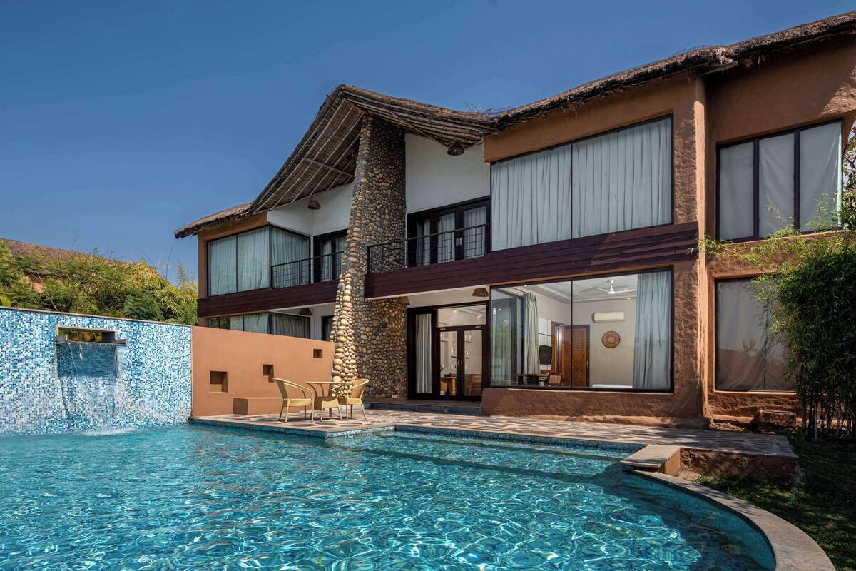 Une maison à deux étages avec une piscine, des piliers en pierre et de grandes fenêtres.