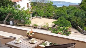 A balcony with wicker furniture and a table, overlooking a garden and a view of the sea.