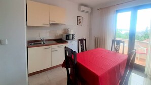A compact kitchen with a microwave, stove, and sink. A dining table with chairs is positioned near a sliding glass door leading to a balcony.