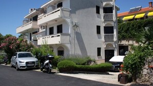 A multi-story building with balconies, parked cars, and greenery.