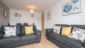 A modern living room with two black leather sofas, each with patterned cushions, a wooden coffee table, and a dining area with a white table and chairs. - Luxury Apt with 2 bathrooms n Free Parking (West Bromwich)