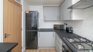 A modern kitchen with white cabinets, a black countertop, a stainless steel refrigerator, a stove, and a toaster. - Luxury Apt with 2 bathrooms n Free Parking (West Bromwich)
