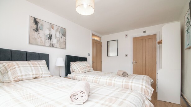 A hotel room with two beds, a large abstract painting, a mirror, and a wooden door. - Luxury Apt with 2 bathrooms n Free Parking (West Bromwich)