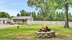 A house with a stone fire pit in the yard, surrounded by a wooden fence and trees.