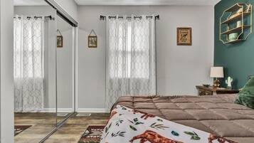 Une chambre avec un grand lit, une porte-fenêtre coulissante et un mur d’accent de couleur verte.