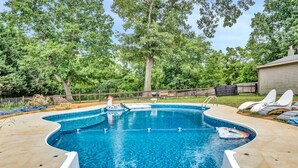 A swimming pool with a unique shape, surrounded by a wooden fence and trees.