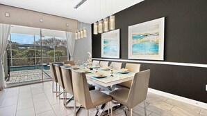 A dining area with a large table set for six, a pool view, and two framed artworks on the wall.