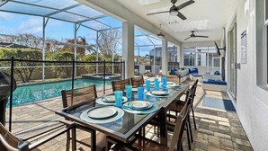 A covered outdoor dining area with a pool view, glass table, and ceiling fans.