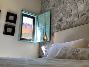 Ein Schlafzimmer mit einer Steinsäule, einem Fenster mit türkisgrünem Rahmen und einer hängenden Leuchte.