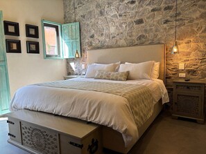 Ein Schlafzimmer mit Steinsturz, einem Bett mit weißer Bettwäsche, einem Nachttisch mit Lampe und einer Kommode mit verzierten Paneelen.