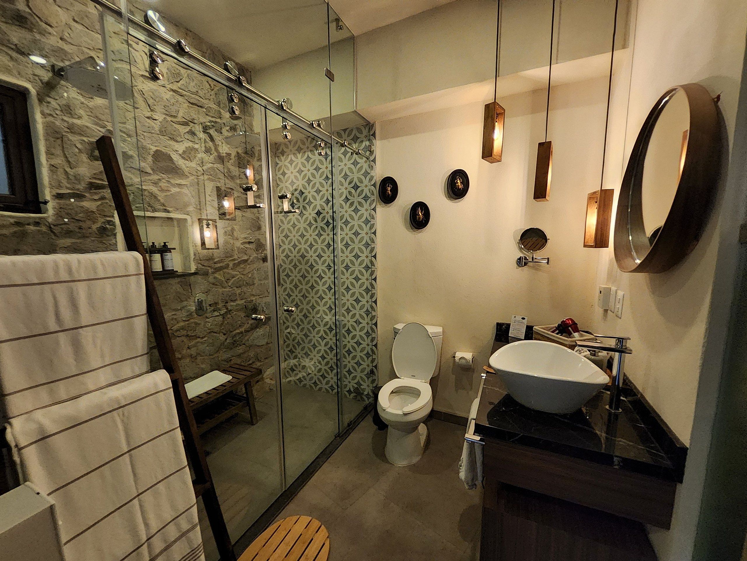 Un baño moderno con ducha envuelta en vidrio, inodoro blanco y un lavamanos grande con espejo superior.