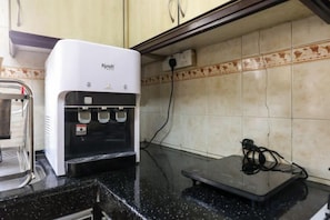 Dispensador de agua con panel de control, balanza y toma de corriente sobre una encimera de cocina.